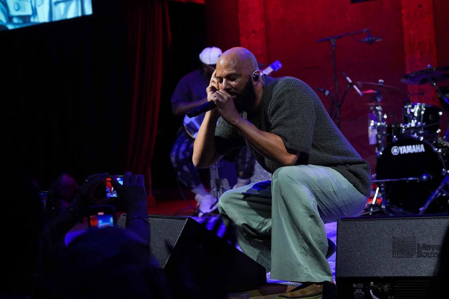 Common raps on stage in front of a large screen displaying "COMMON 2025 Belafonte Fellow."
