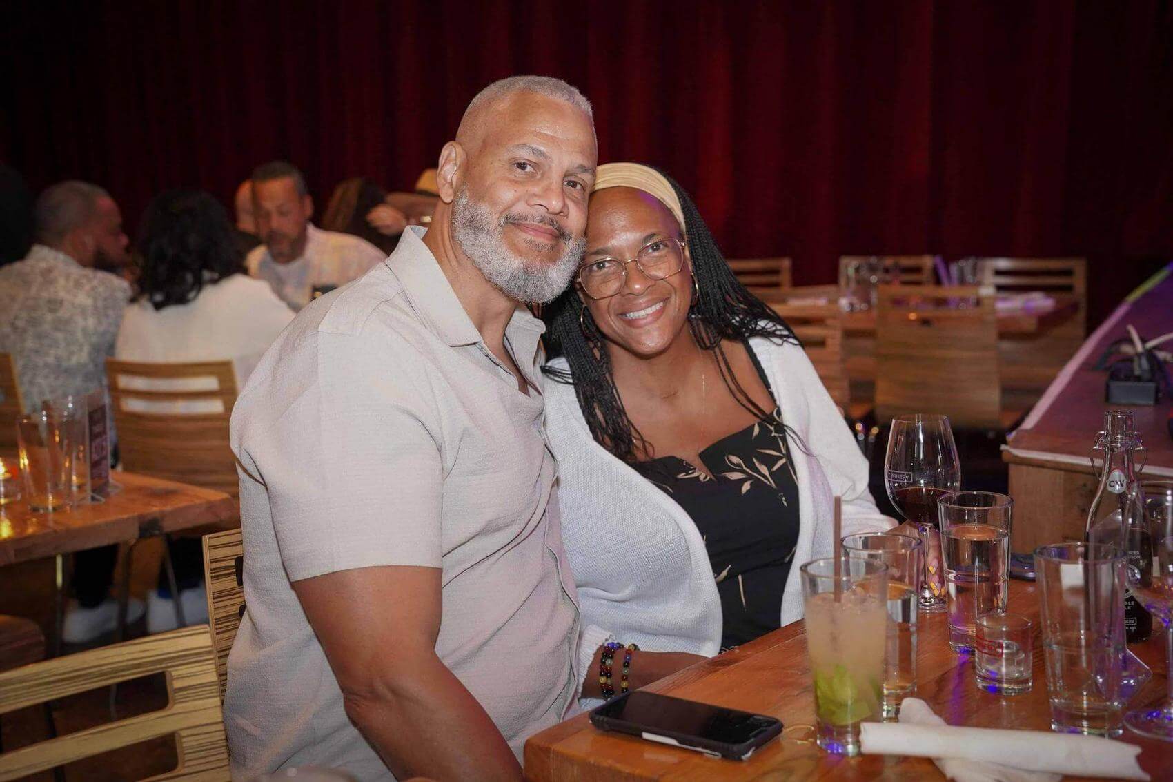 Two men pose together in a crowded venue, one with a fist raised and the other wearing sunglasses.