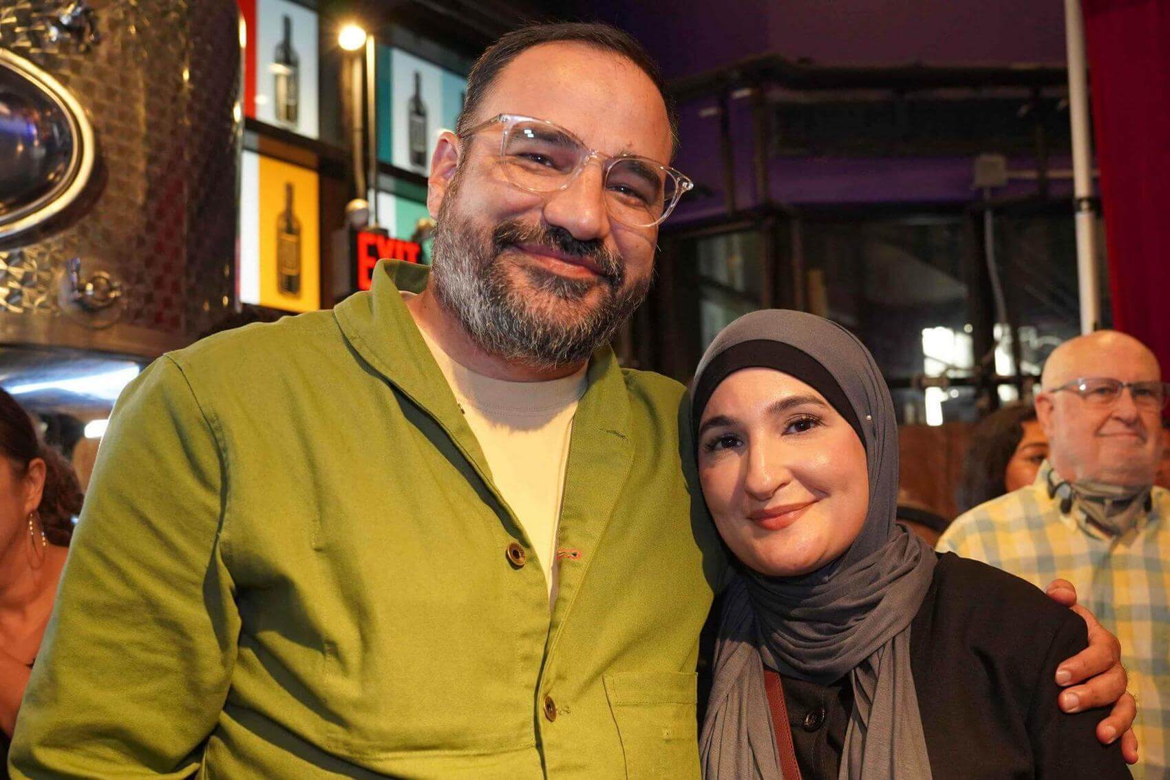 Lemon Andersen speaks on stage with a microphone, a screen displaying his name in the background.