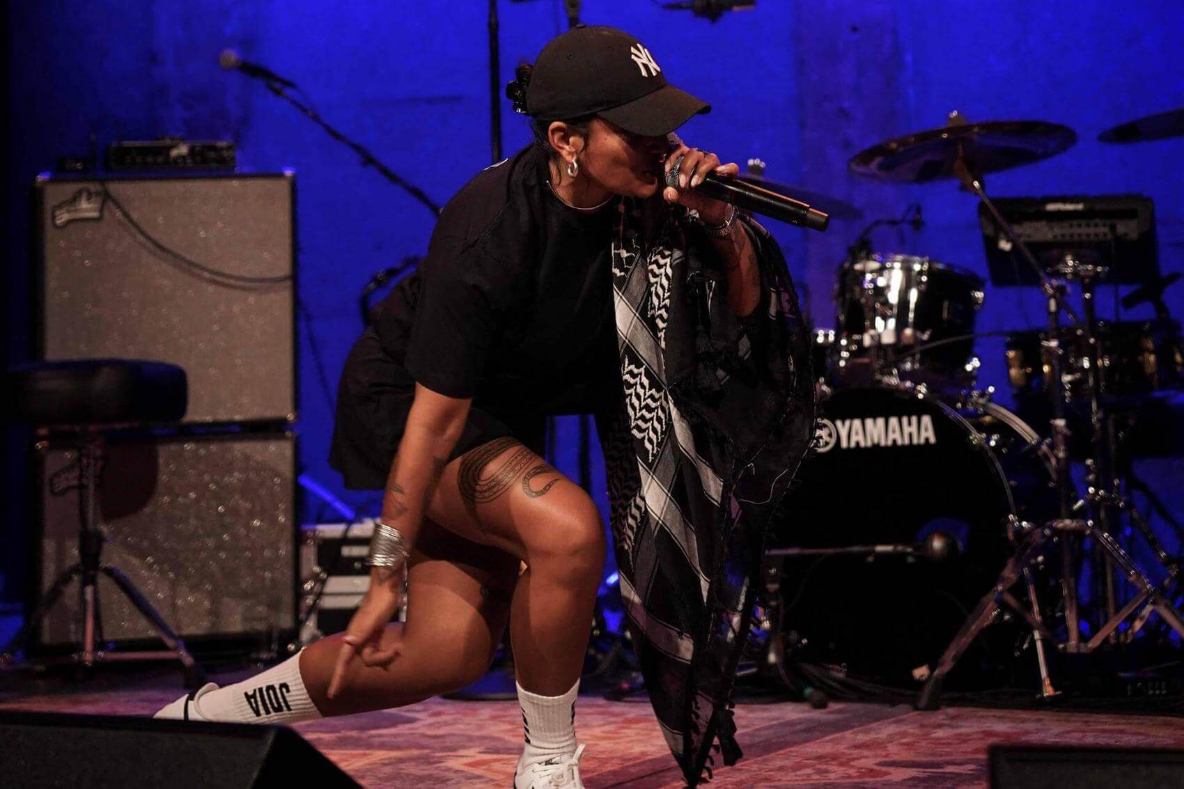 Seated crowd in a dimly lit venue with screens showing a photo of a woman.