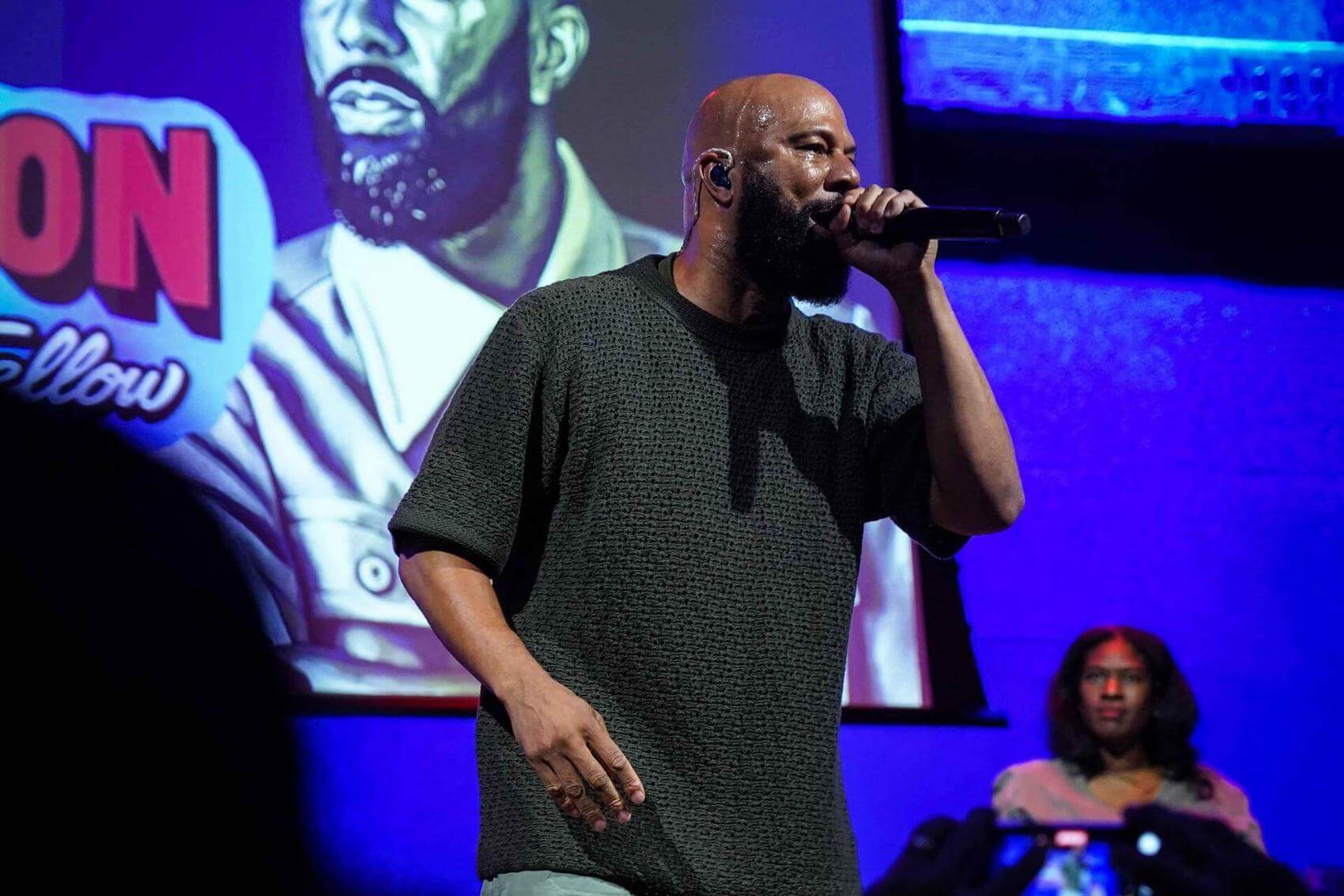 Ana Tijoux holding a microphone with one hand raised during a performance.