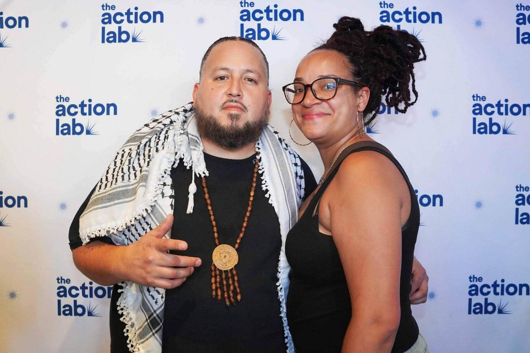 Two men sit at a table with drinks, posing for the photo with peace signs.