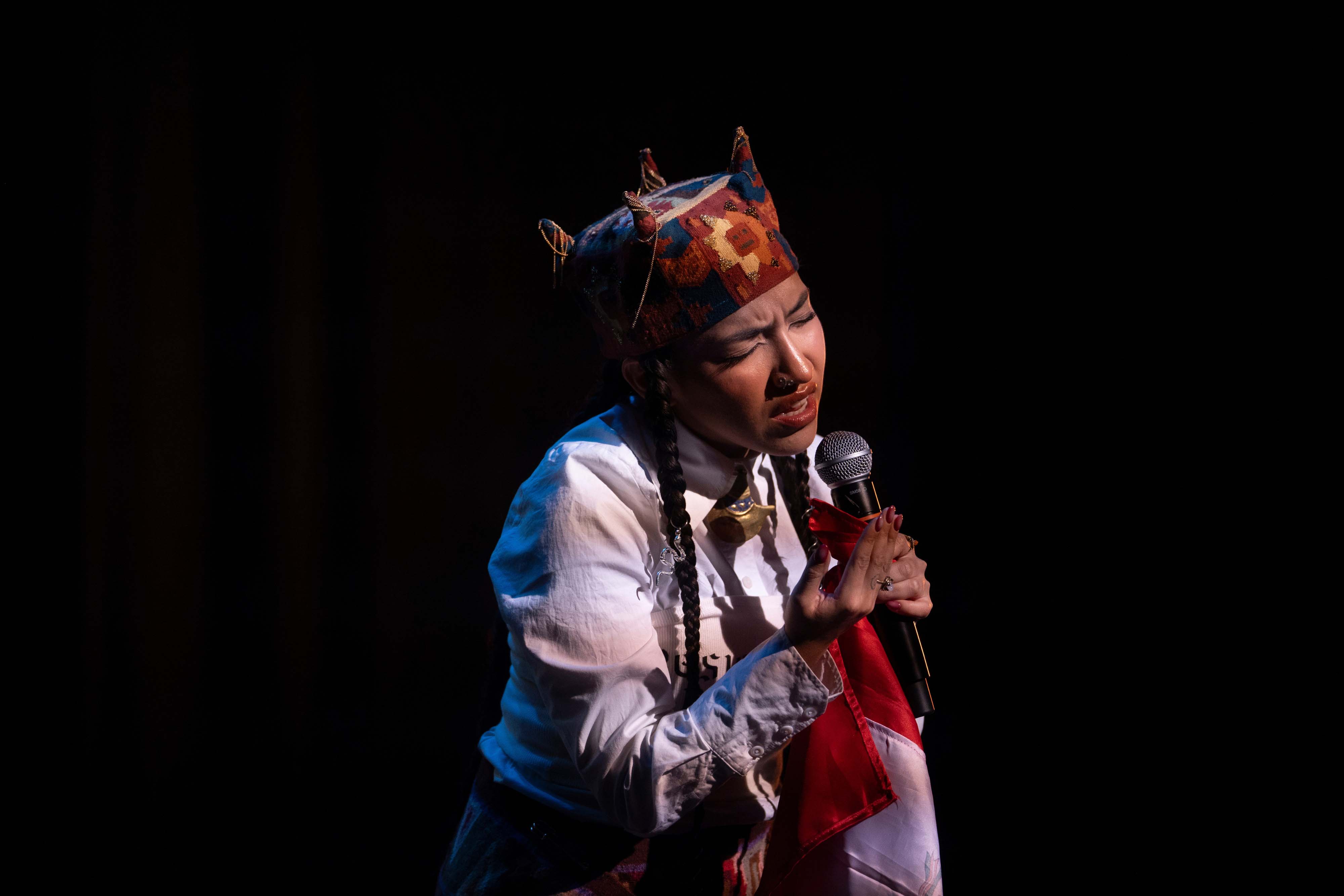 Performer on stage with raised hand in front of a cheering crowd and bright lights.