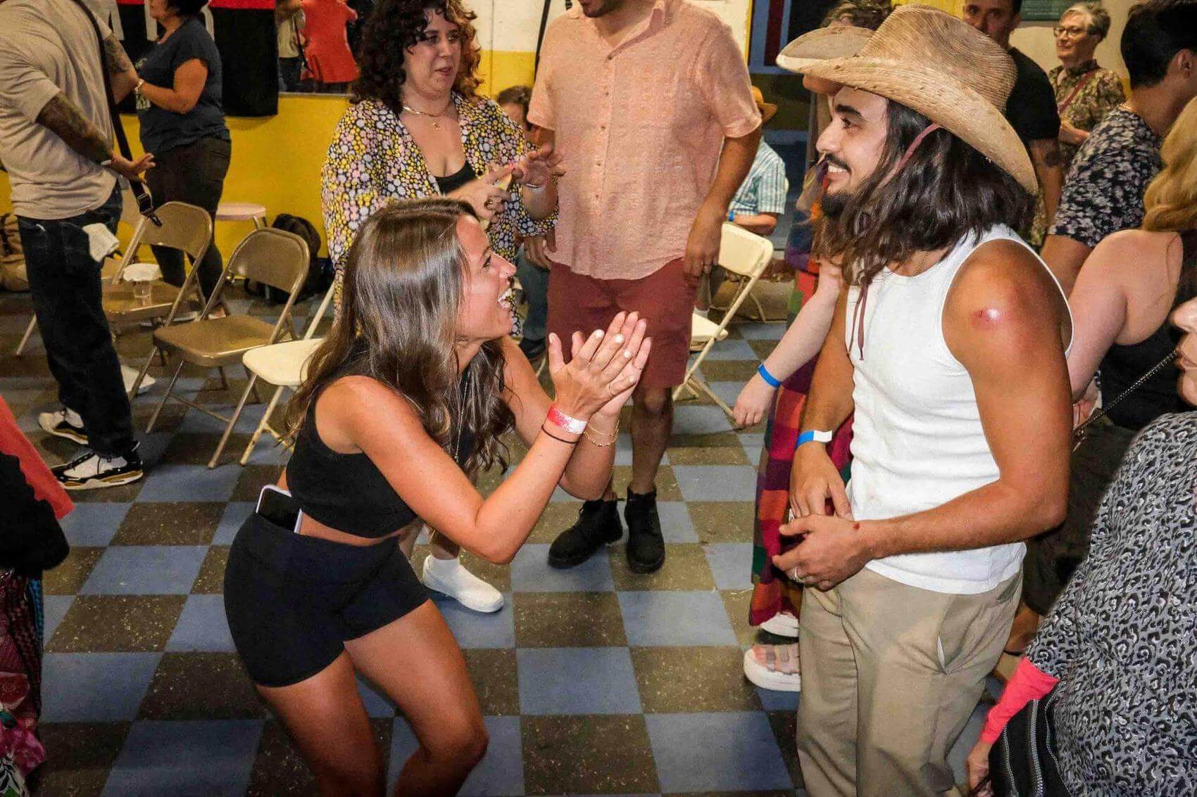 Group of people socializing and laughing in a casual setting. Some hold drinks.