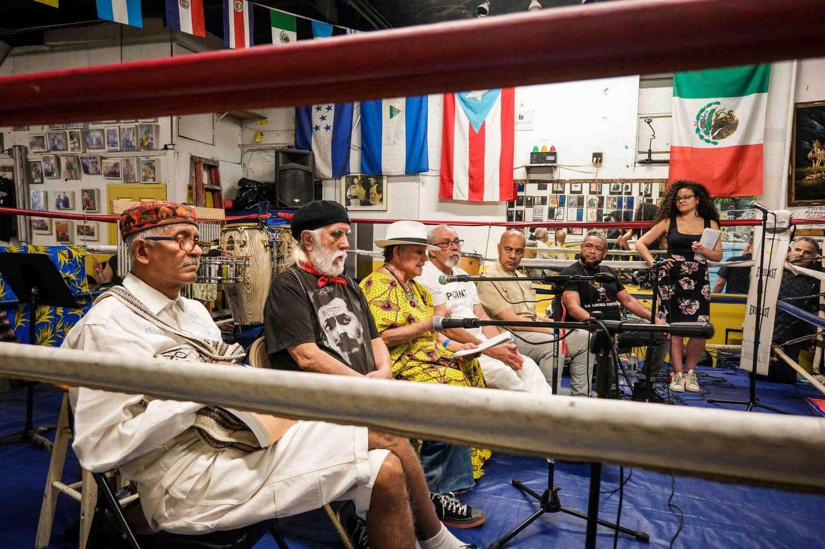 Group of people dancing and enjoying music in a venue with a boxing ring and flags.