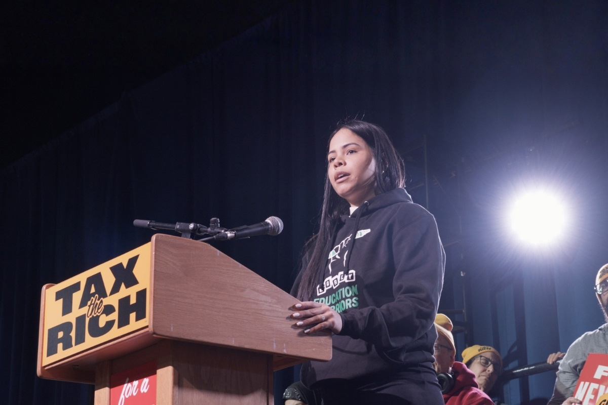 People holding banners and signs with text "Tax the Rich" and "Stand up to Trump" during a protest.