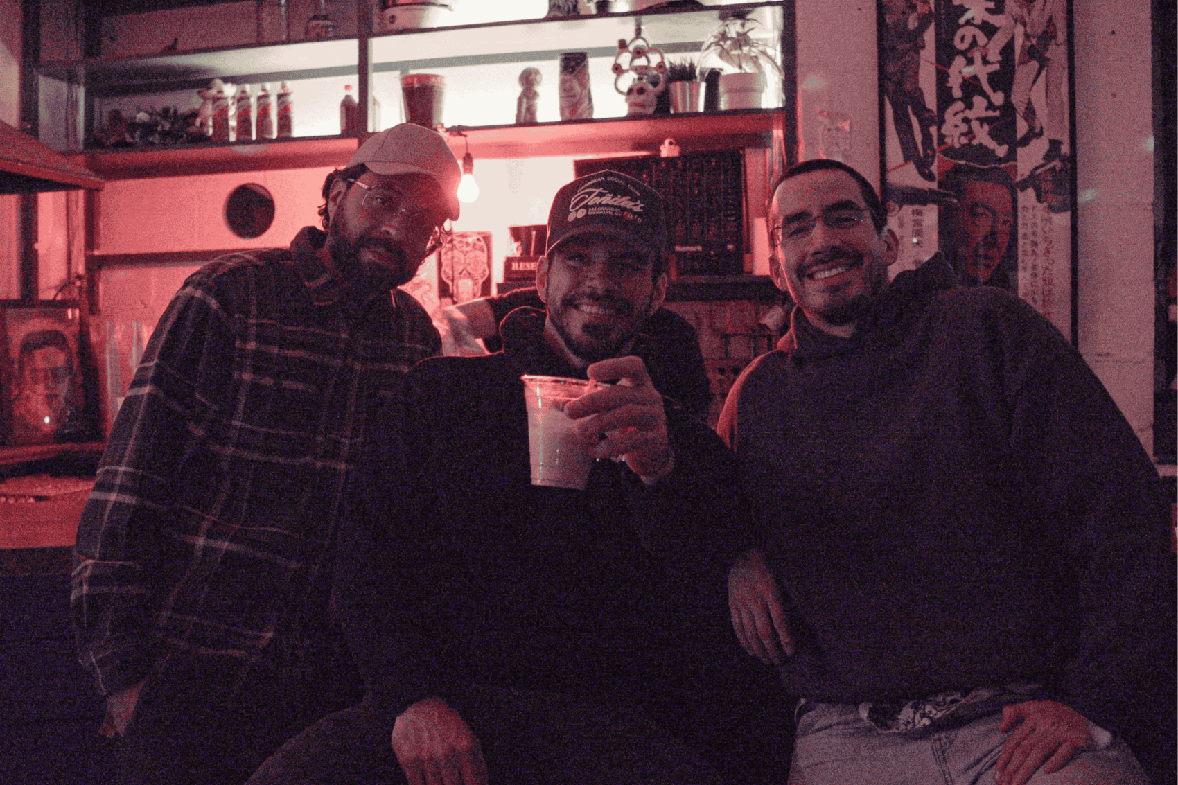Three men smiling, one holding a drink in a plastic cup