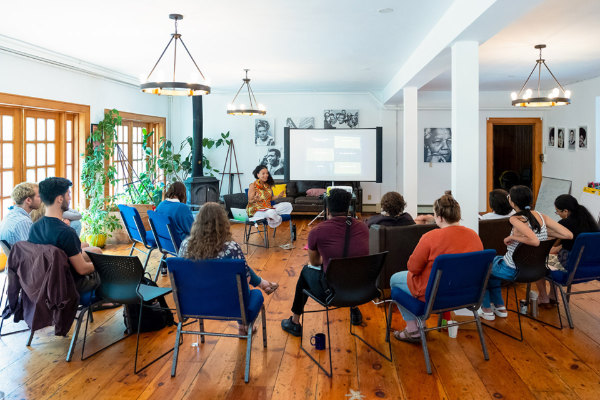 Facilitator leads a small group workshop in a bright room with seated attendees.