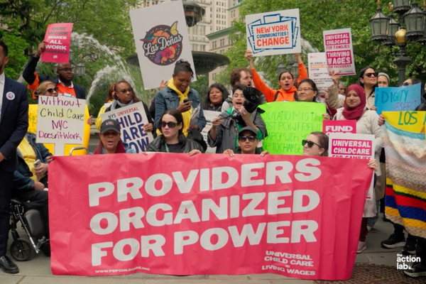 Child care providers and advocates rally in New York City behind a “Providers Organized for Power” banner demanding universal child care and living wages.