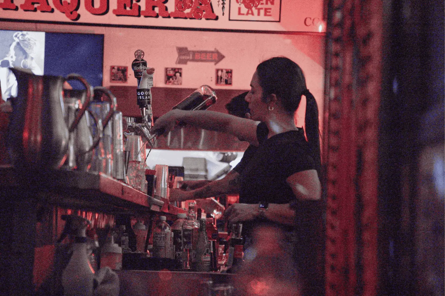 Bartender pouring beer from a tap into a plastic cup behind a bar.