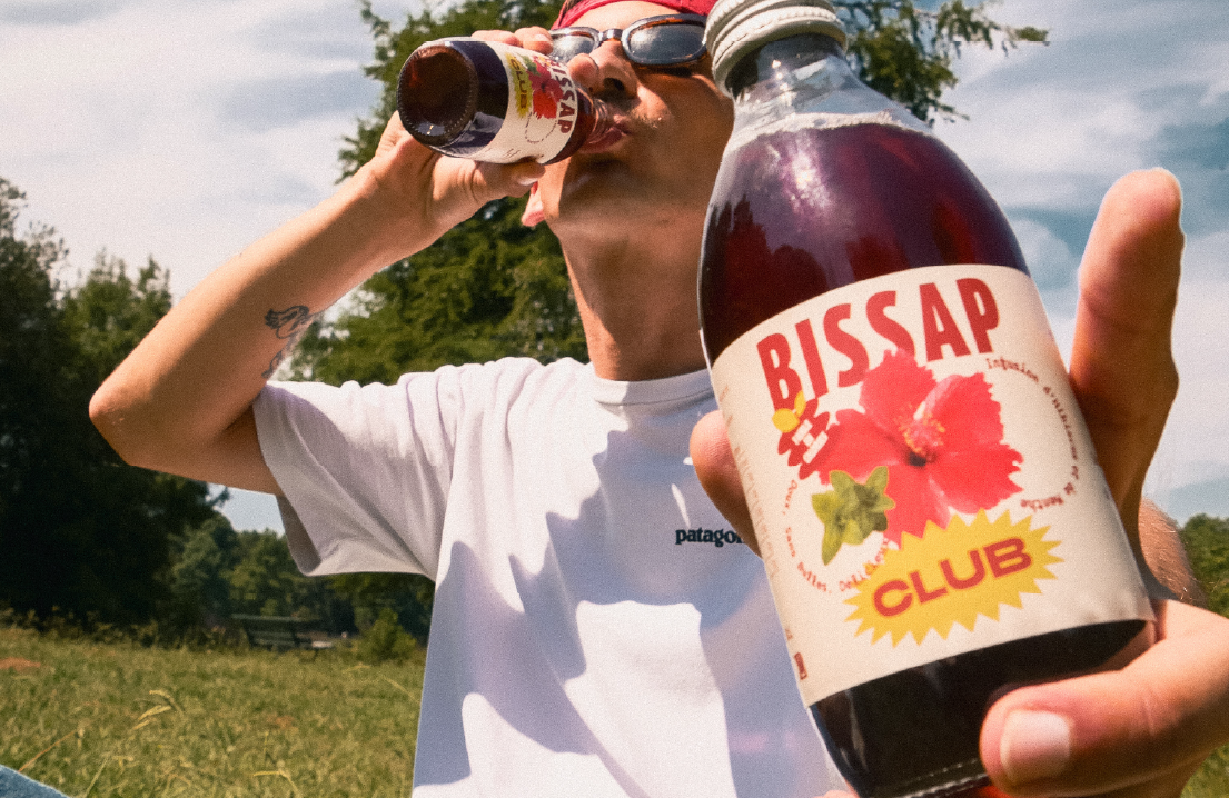 Un homme qui tient la bouteille de Bissap Club en gros plan et l'autre main avec la bouteille à la bouche