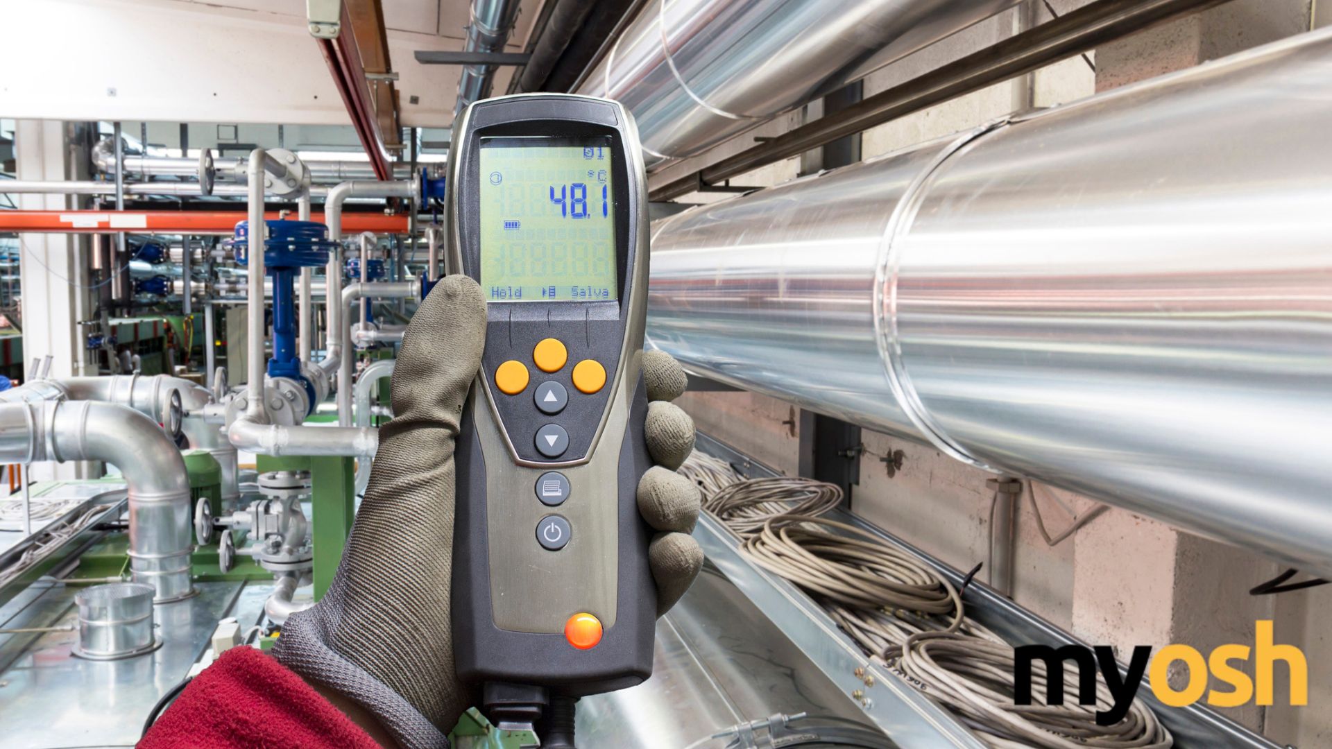 Worker using a handheld air monitoring device near industrial piping to measure workplace air quality and potential airborne contaminants.