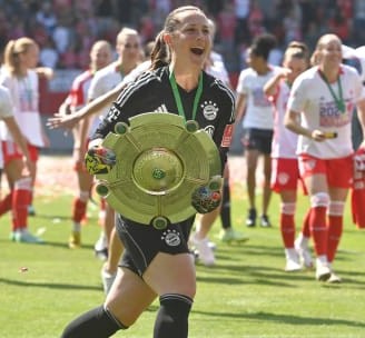 Fußballtorfrau Laura Benkarth trägt die Meisterschale und feiert mit ihrer Mannschaft auf dem Spielfeld.