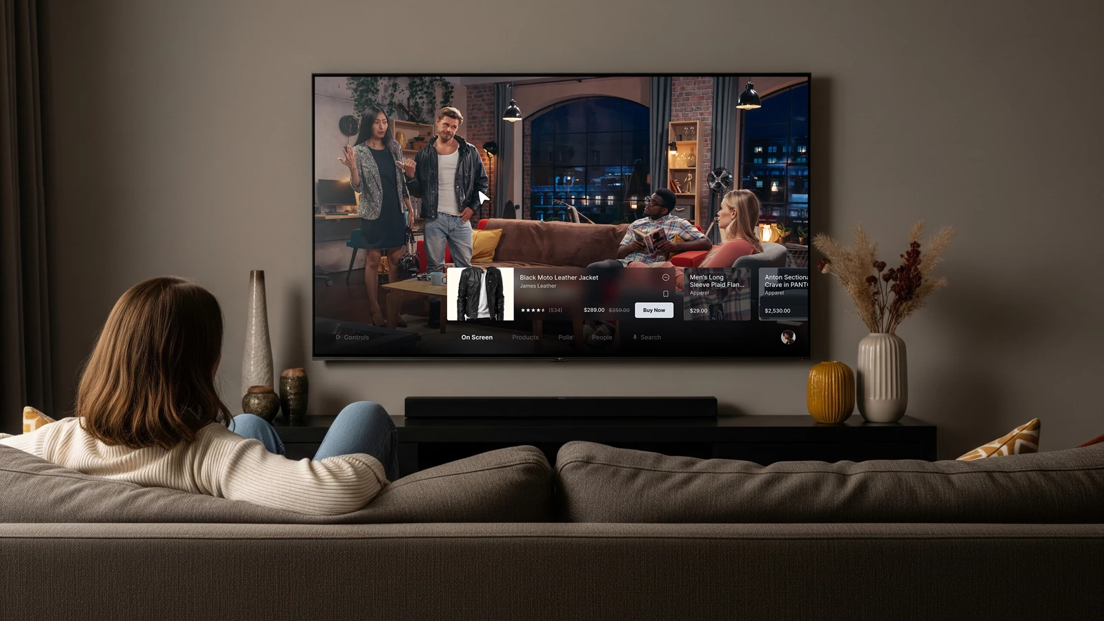 Woman in cream sweater sitting on a couch watching a smart TV with an interactive shopping interface displaying a leather jacket and other apparel in a modern living room.
