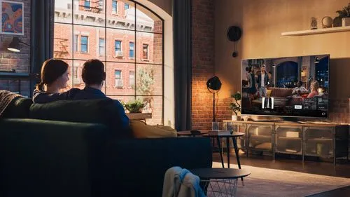 Couple sitting on a dark green couch watching a smart TV mounted on a brick wall in a cozy living room.