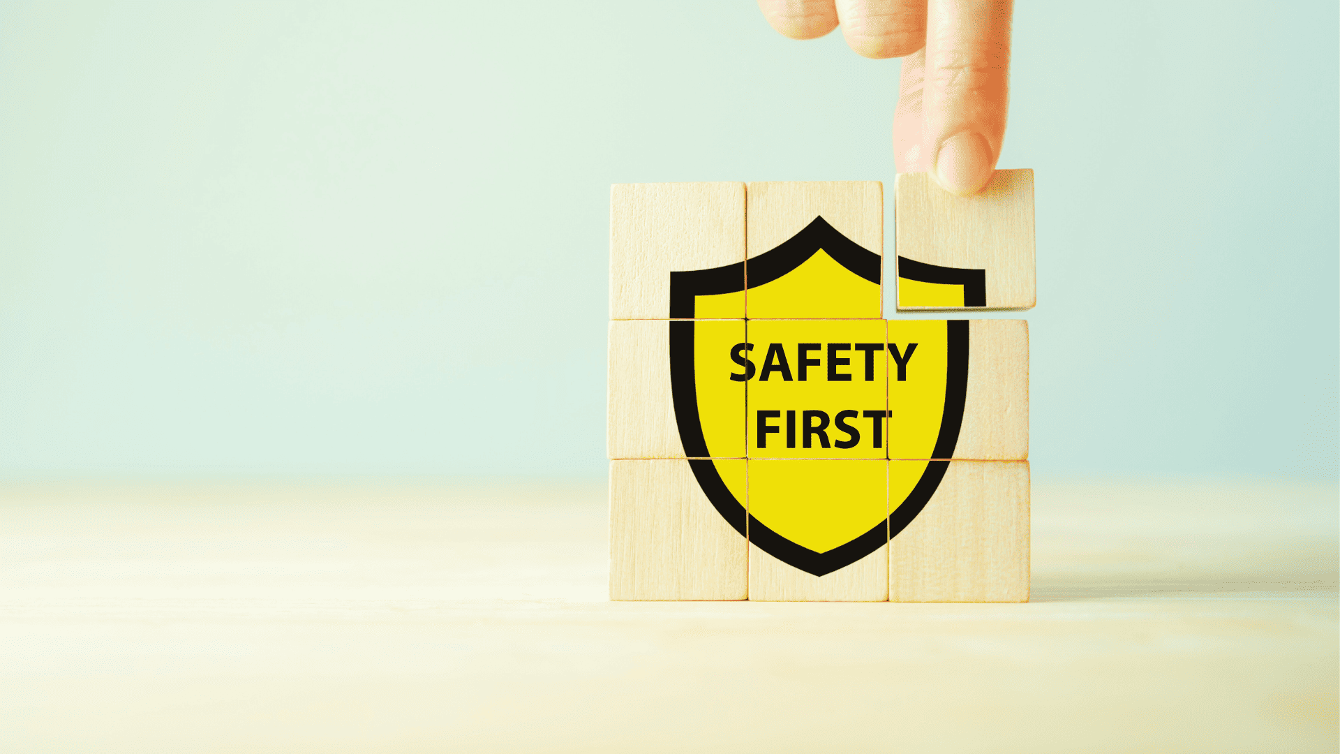 Main plaçant un bloc en bois sur un puzzle formant un bouclier jaune avec le texte « Safety First », illustrant l’importance du repérage amiante avant travaux (RAAT) pour garantir la sécurité sur les chantiers et prévenir les risques liés à l’amiante.