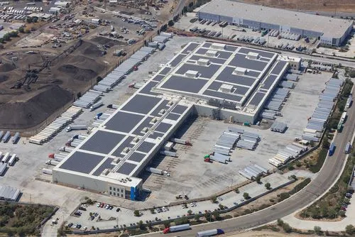 Aerial view of a large Lineage logistics warehouse with solar panels on the roof and numerous trucks parked around.