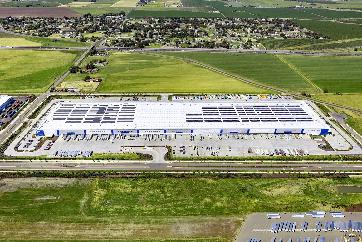 Aerial view of a large Medline warehouse with solar panels on the roof, surrounded by fields and parking lots with trucks.