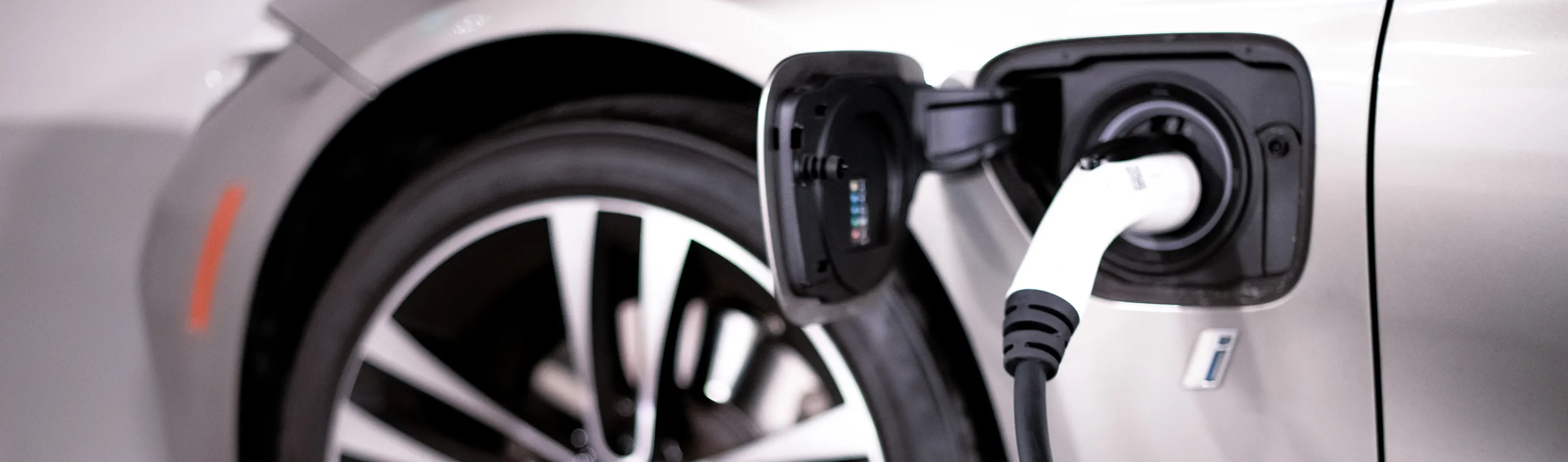 Close-up of a silver electric car plugged into a charging station near the rear wheel.