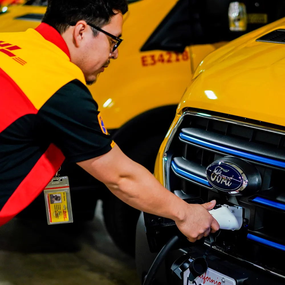 Man wearing a DHL uniform charging a yellow Ford electric vehicle.