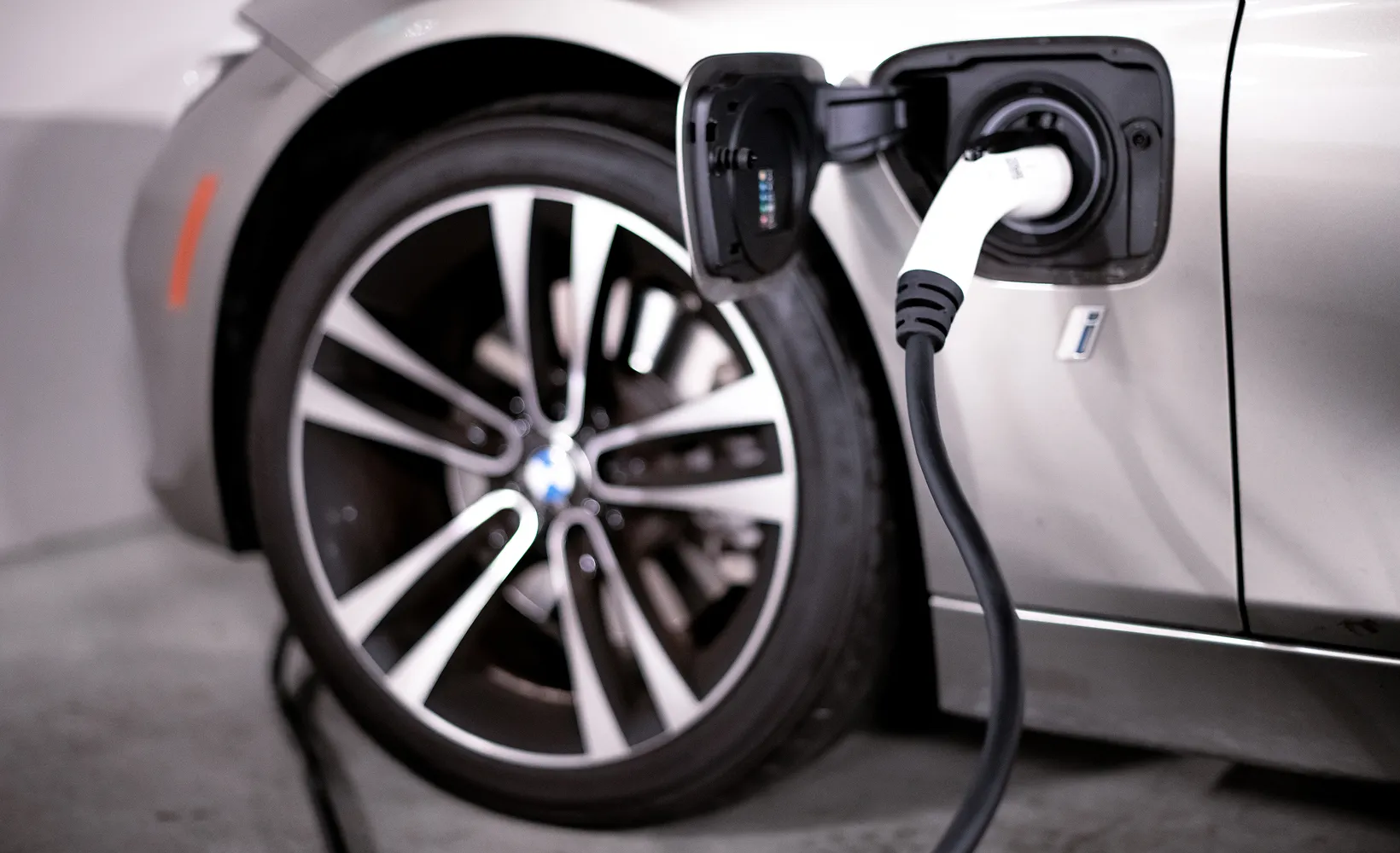 Close-up of a silver electric car charging with a cable plugged into the port near the rear wheel.