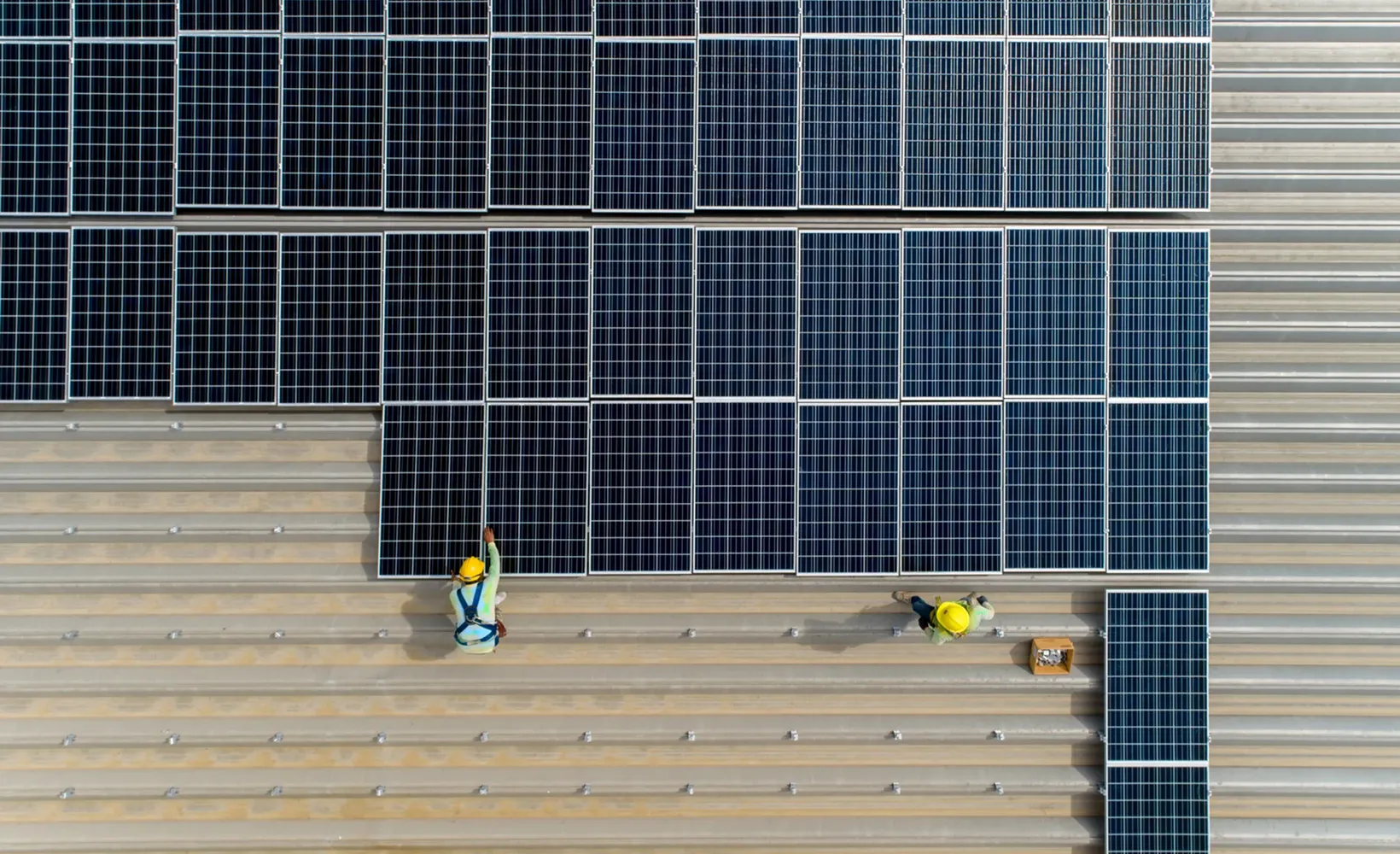 Two workers installing solar panels on a metal rooftop viewed from above.
