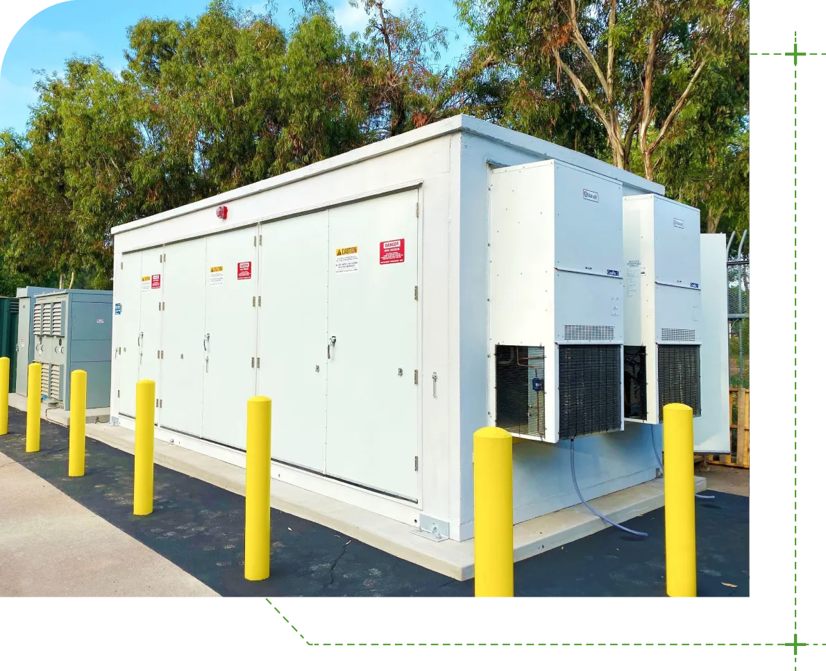Large white outdoor battery energy storage unit with yellow bollards and surrounded by trees.