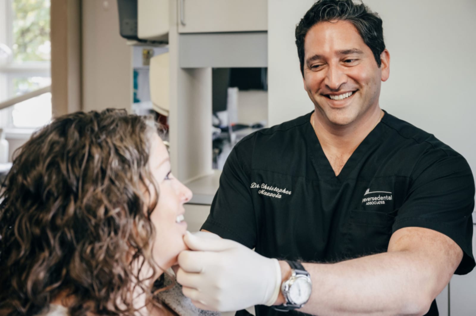 Male dentist in black scrubs performing dental procedure on patient in clinical setting