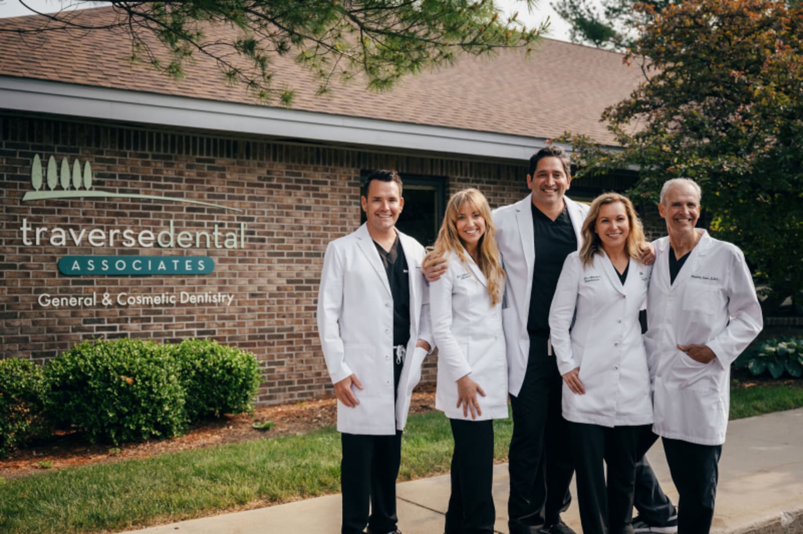 Team of dental professionals in white coats standing together outside