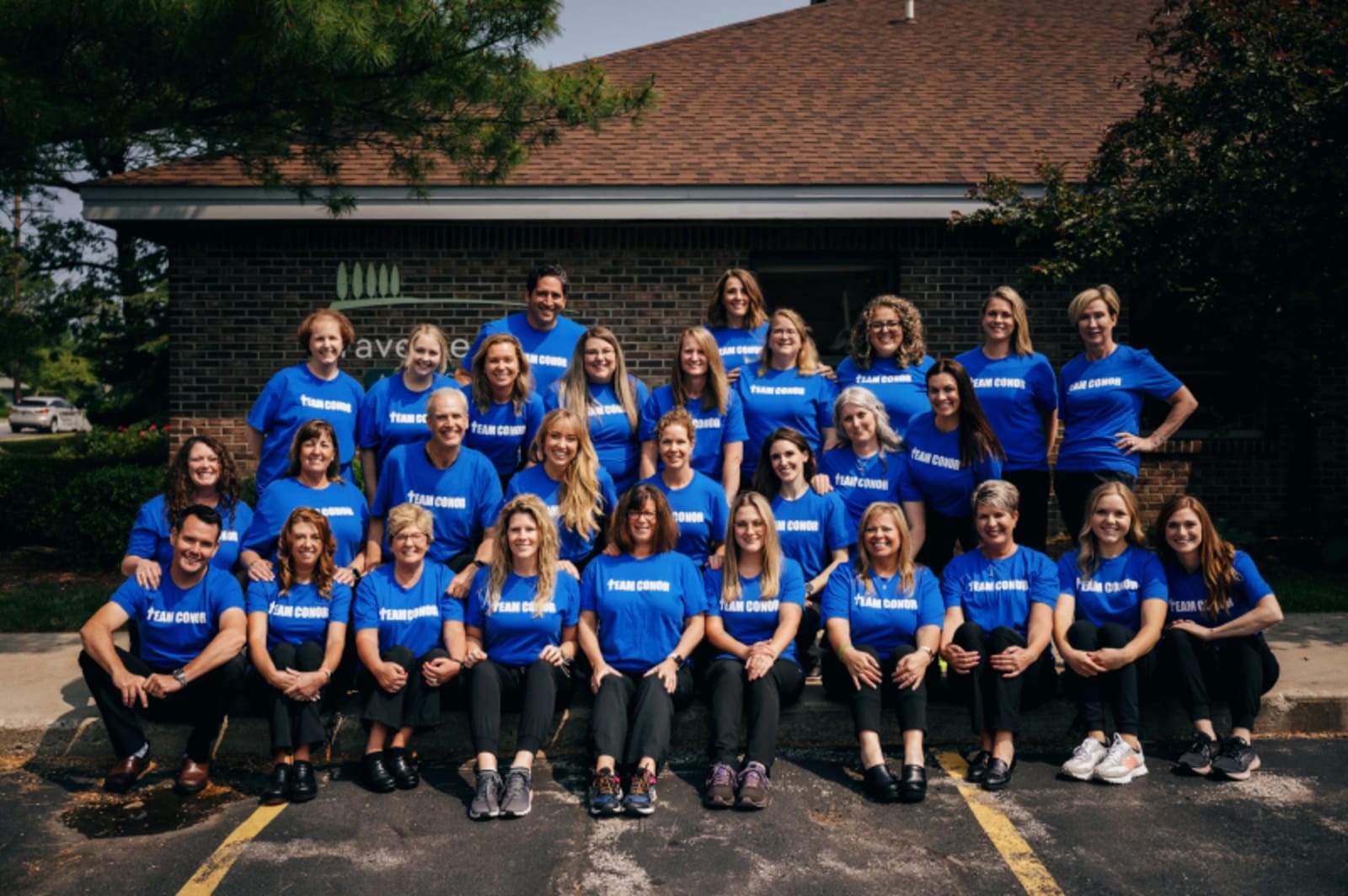 Large group photo of dental practice team in blue shirts standing together outdoors