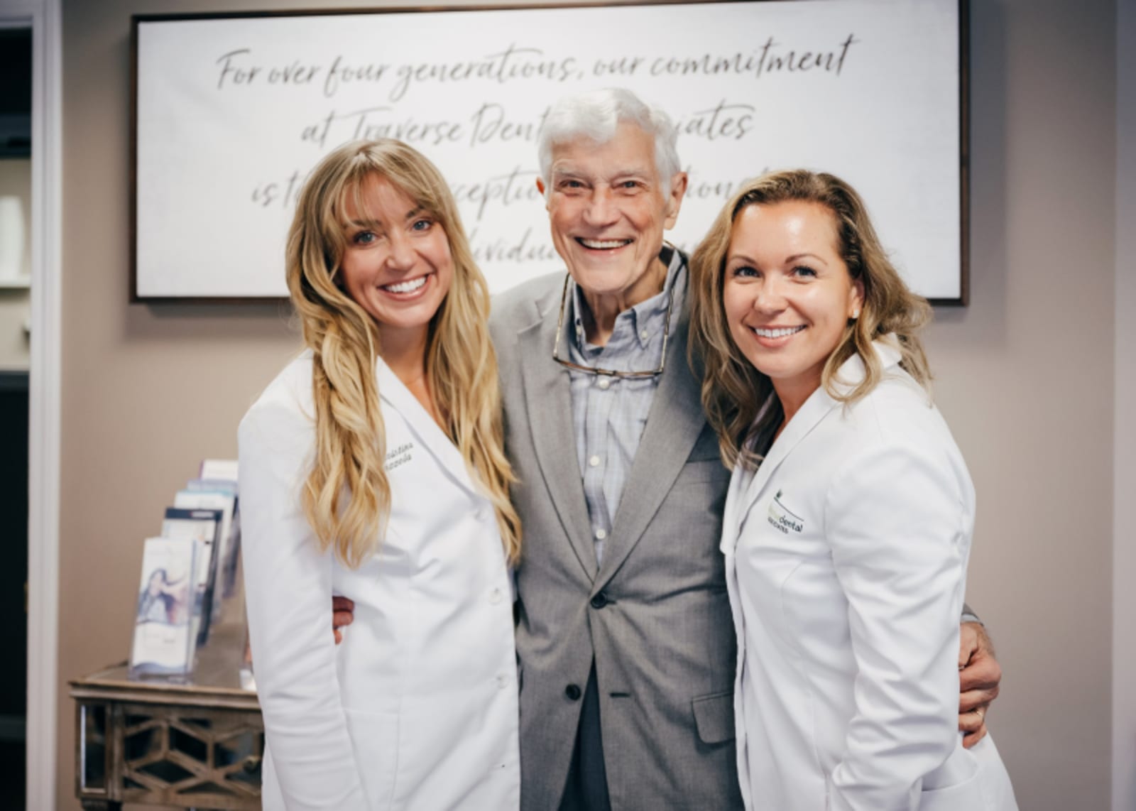 Three dental professionals in white coats smiling together in office setting