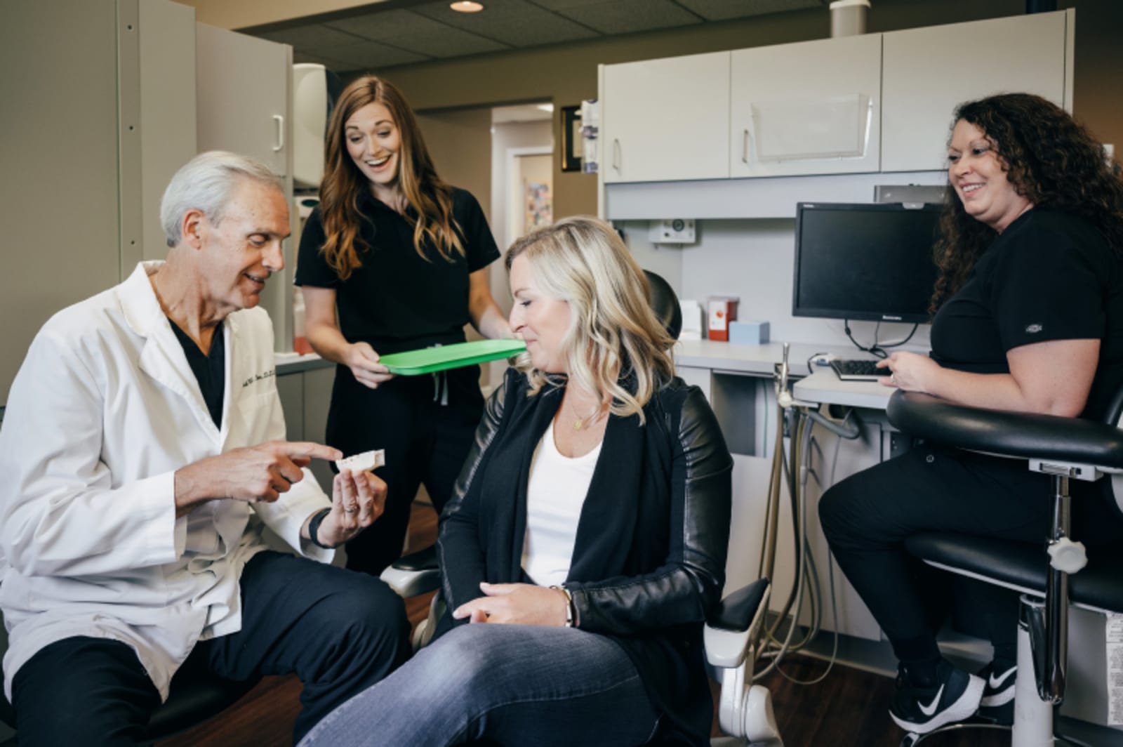 Multiple dental professionals gathered around patient in clinical office discussing treatment