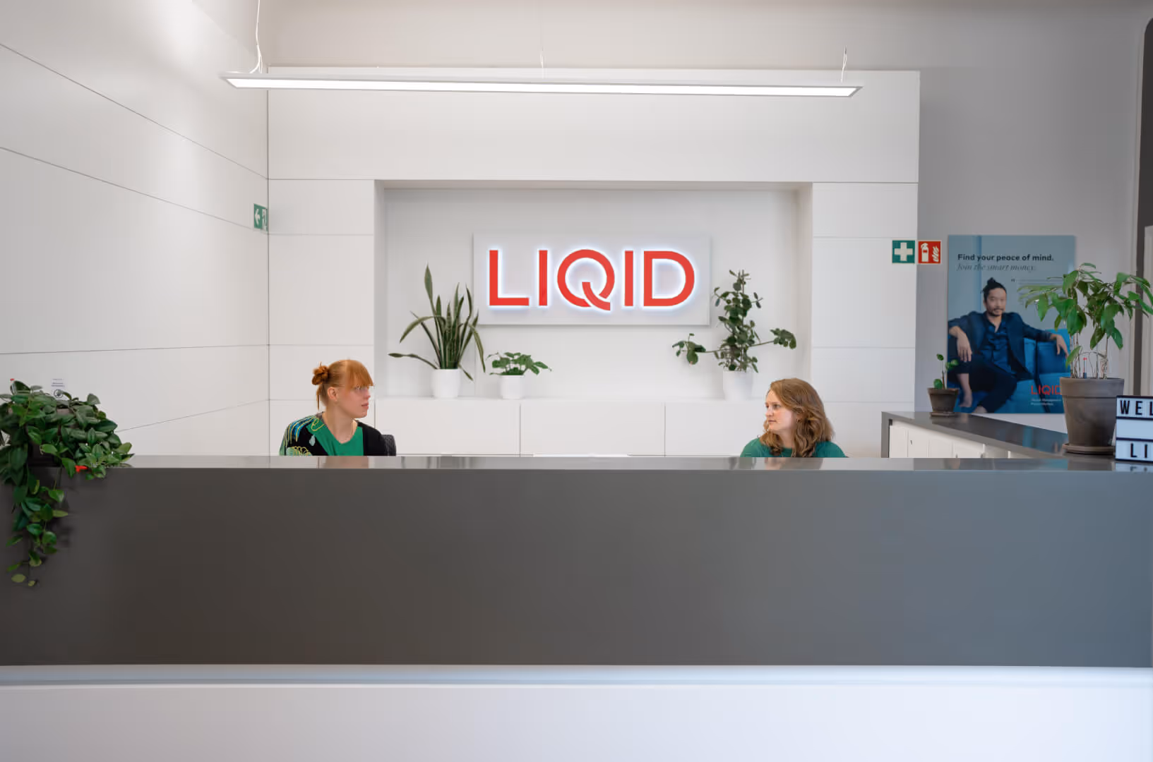 Rezeption von Liquid mit Firmenlogo, Pflanzen und zwei Mitarbeitern
