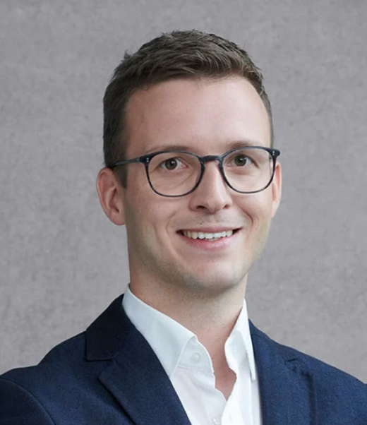 Moritz von Rhein mit Brille im blauen Anzug vor grauem Hintergrund