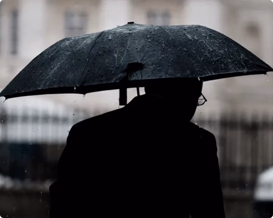 Schwarze Silhouette mit Regenschirm an einem regnerischen, trüben Tag