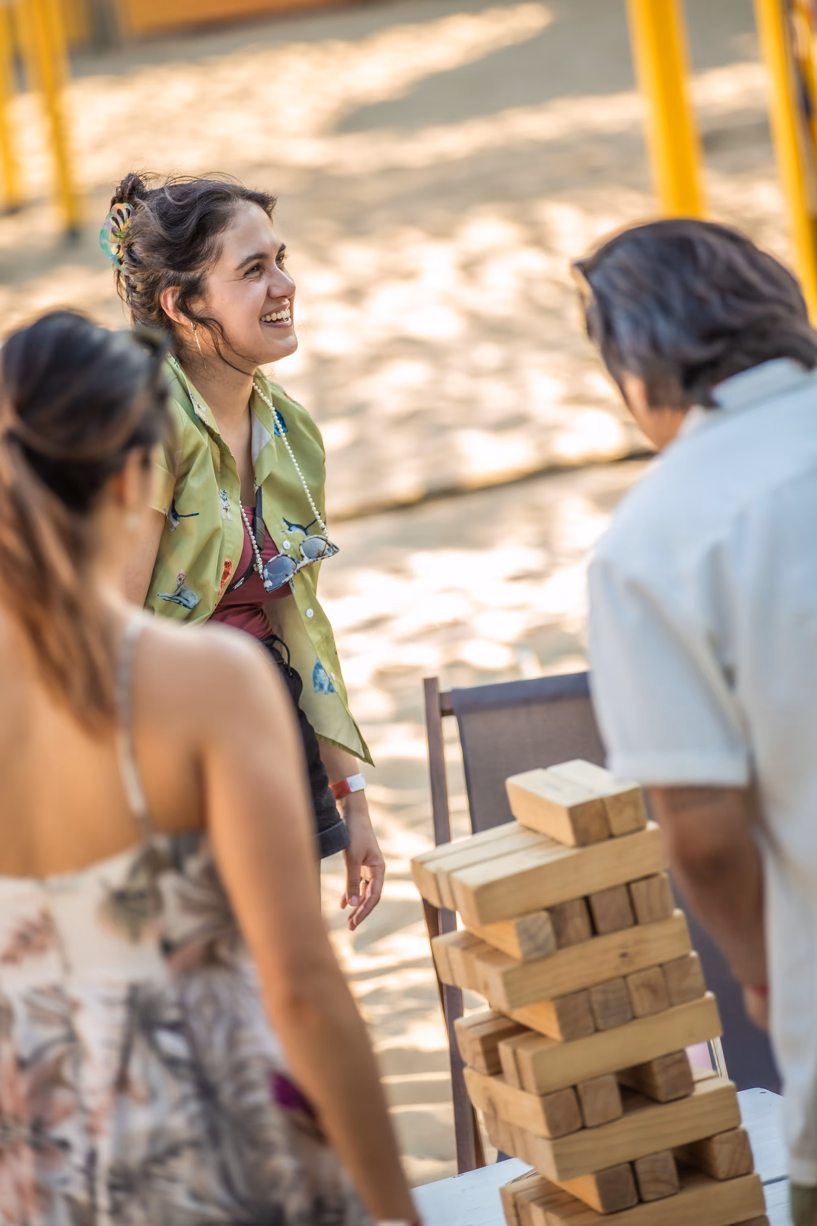 Freunde spielen Jenga-Spiel draußen, lachende Person in grüner Jacke