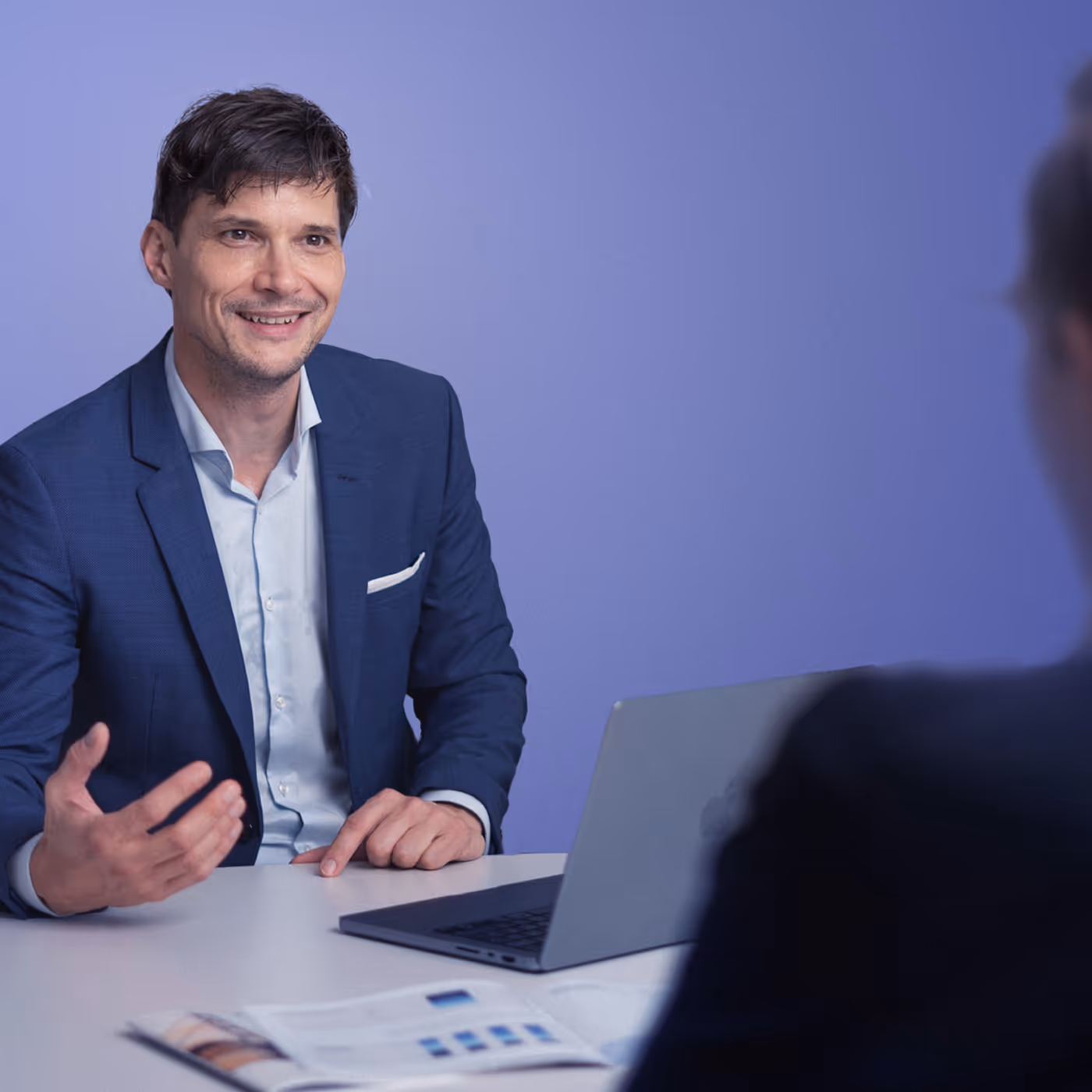Lächelnder Geschäftsmann im blauen Anzug während eines Gesprächs am Laptop