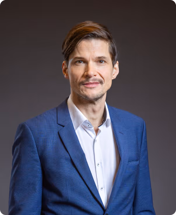 Mann im blauen Blazer lächelt freundlich vor grauem Hintergrund