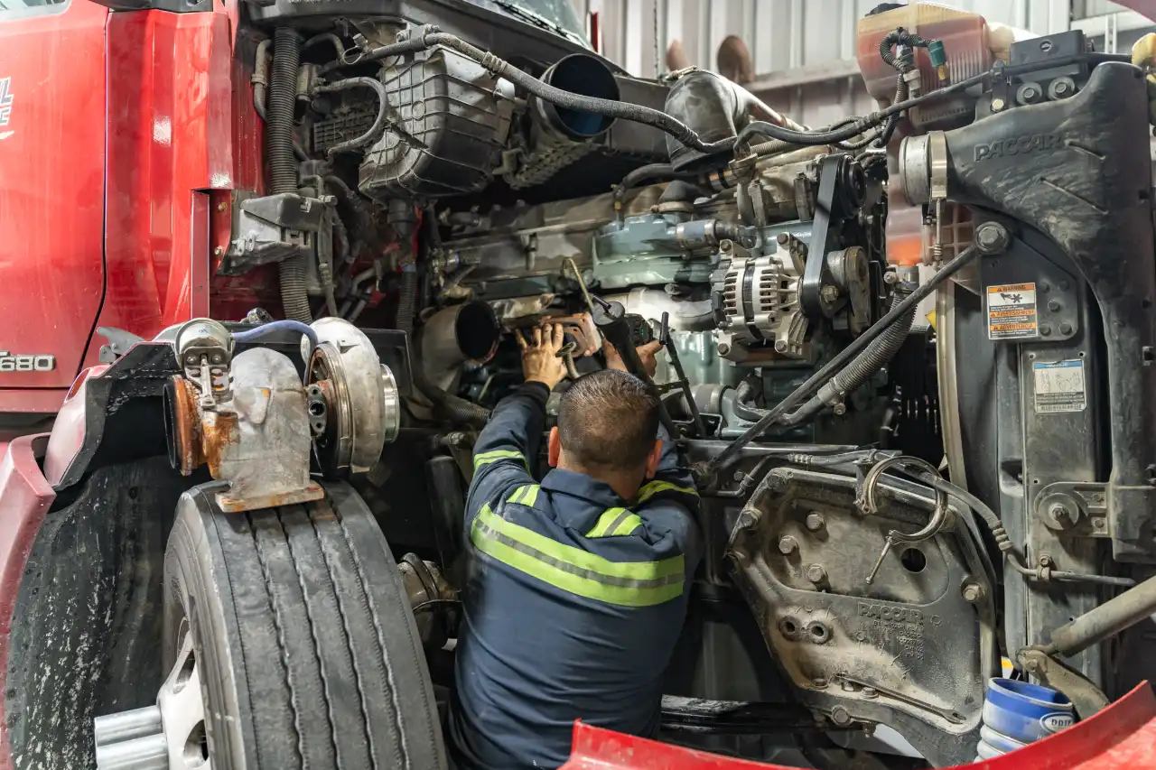 Mechanic performs heavy-duty engine repair on Kenworth T680; turbo, alternator and PACCAR radiator exposed.
