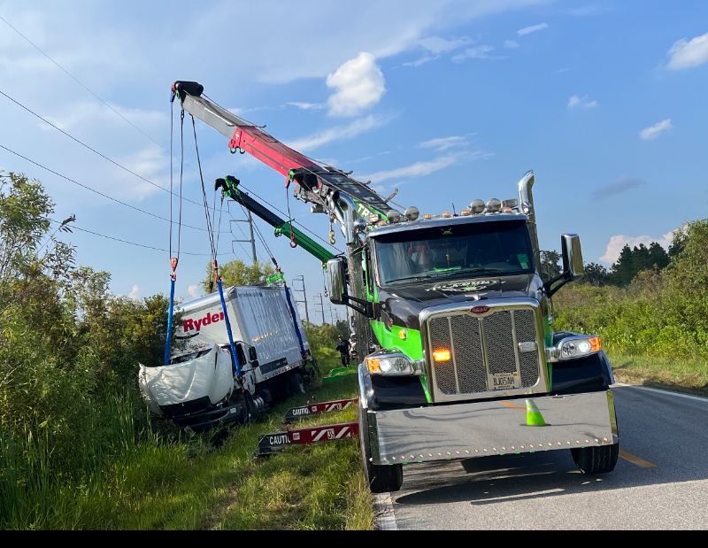 Two heavy-duty mobile cranes recover a damaged Ryder box truck from a grassy roadside ditch, ensuring a safe and controlled lift.