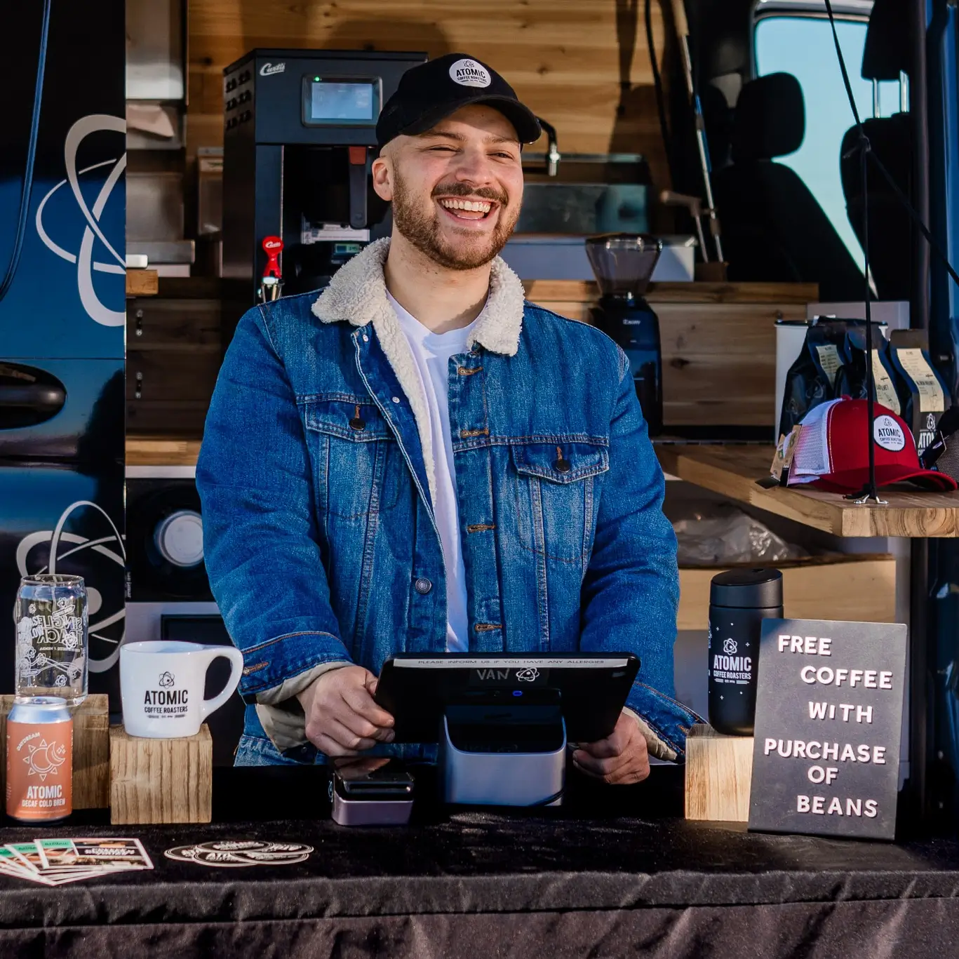 Smiling barista at a coffee stand, showcasing products and promoting community through coffee experiences.