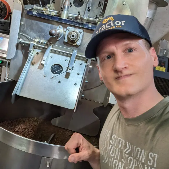 Matt, owner of City Boy Coffee, poses in front of a coffee roaster, showcasing his passion for specialty coffee.