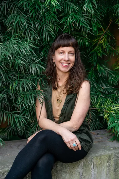 Crystal Marie Higgins, a High Priestess and herbalist, smiles warmly among lush greenery, embodying earth wisdom.