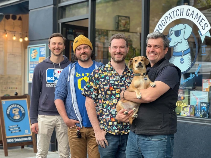 A team of board game enthusiasts and a dog, smiling outside Dogpatch Games, showcasing their community spirit.
