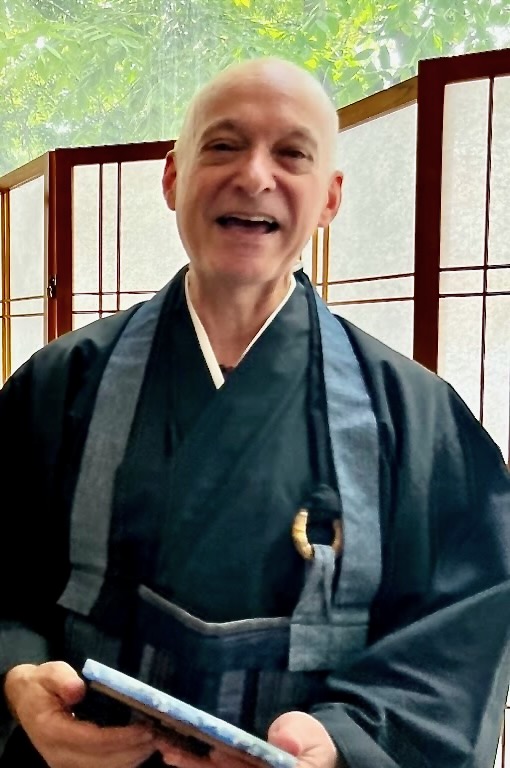 Smiling host in traditional attire, holding a book, amidst a serene, peaceful setting with natural light.