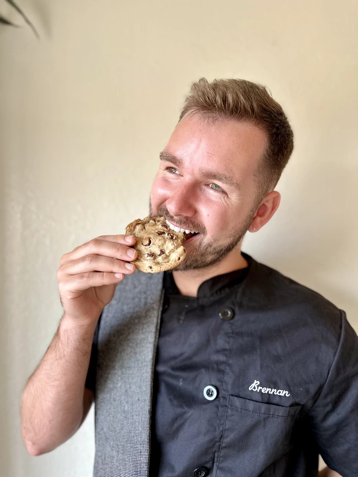 Brennan, a baker, smiles while holding a cookie, ready to share his passion for desserts with others.