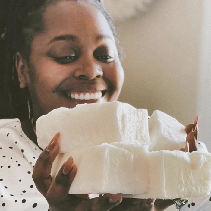 Smiling woman holds large pieces of white material, showcasing her passion for fragrance and candle making.
