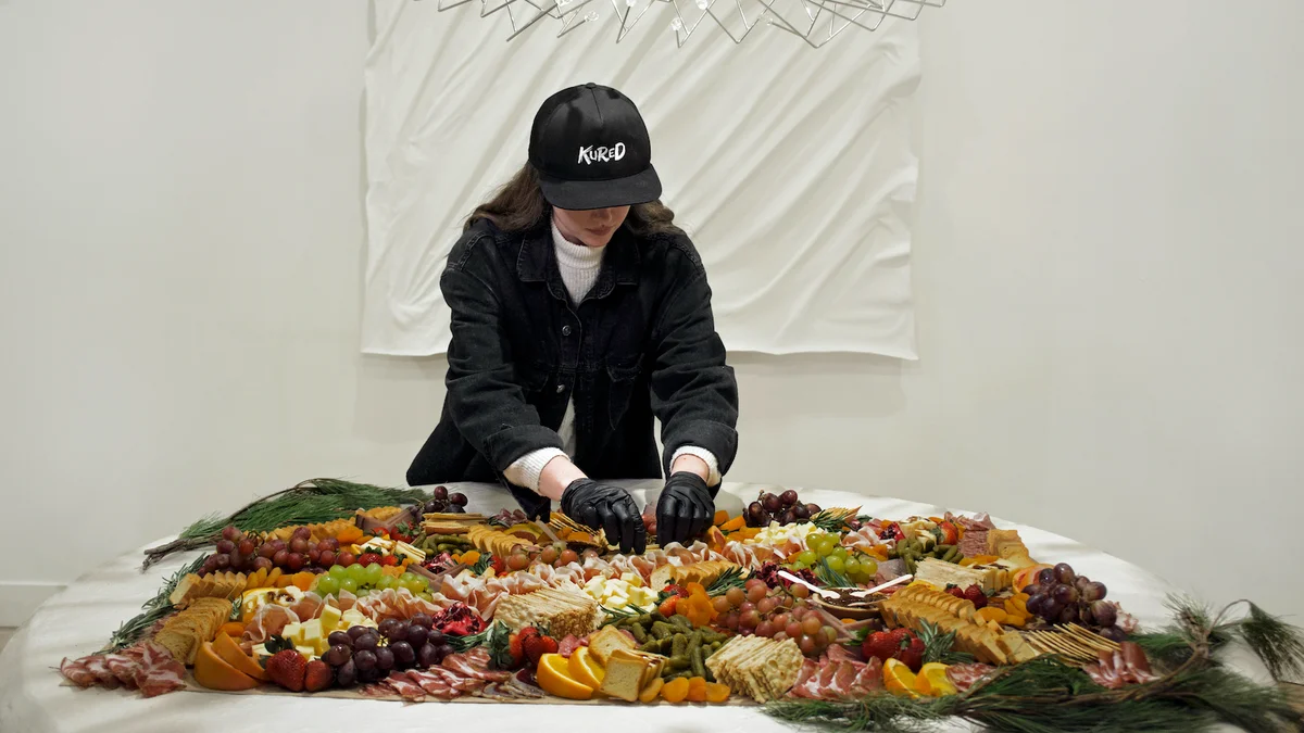 A woman arranges a colorful charcuterie spread on a table, showcasing meats, cheeses, and fruits in an elegant setting.