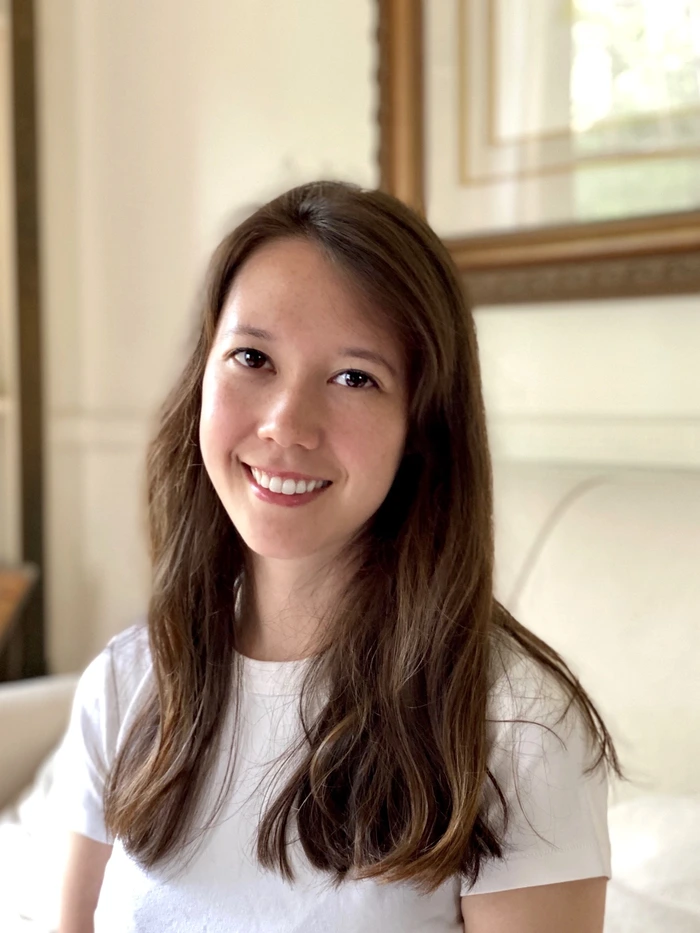Portrait of a woman with long hair, smiling warmly, in a cozy environment, representing a certified aromatherapist and meditation instructor.