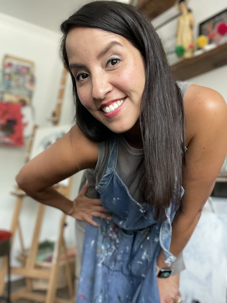 Portrait of Margaret, a working artist in an apron, smiling in her art studio filled with creative supplies.